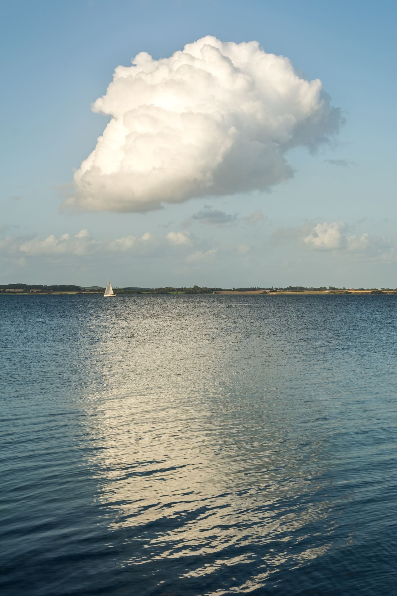 Blick über's Wasser auf Küste, große Wolke spiegelt sich im Wasser